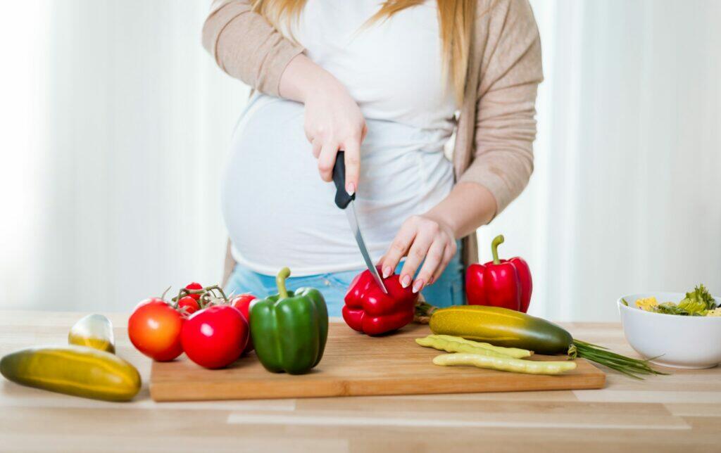 Pregnant woman preparing salad and cutting vegetables